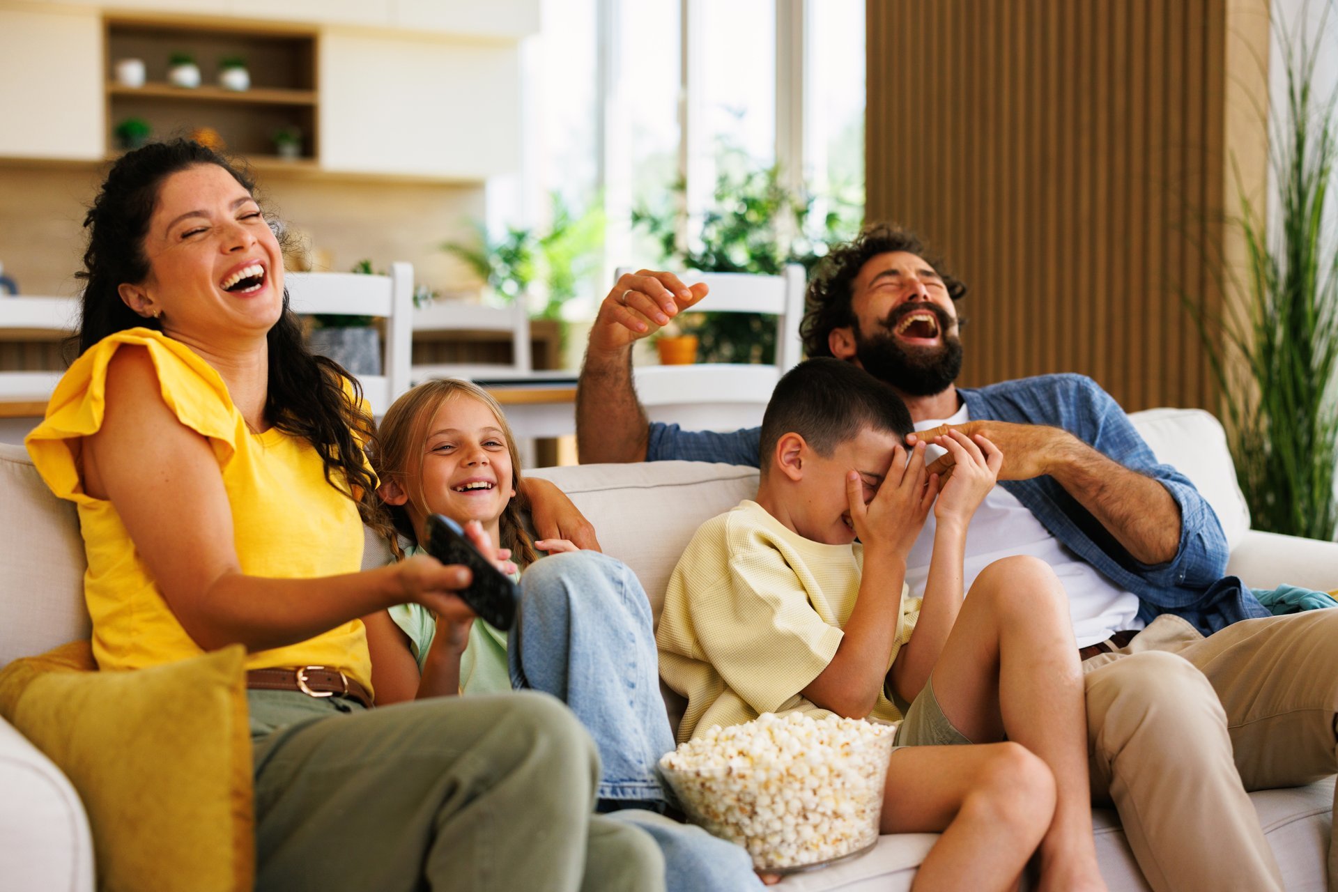 Cheerful family enjoying a funny movie night at home, laughing and eating popcorn